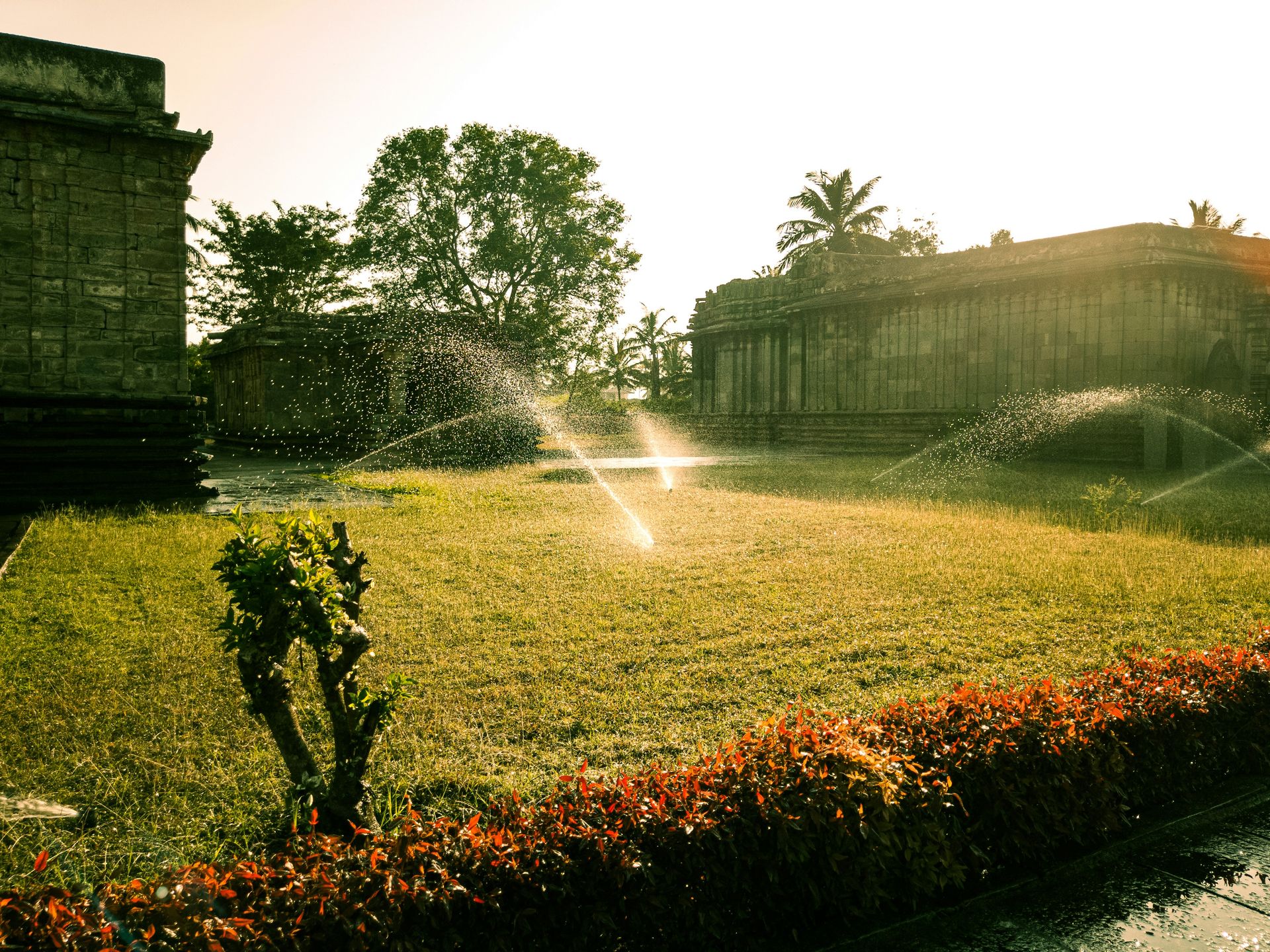 Sprinklers watering a grassy area near old buildings.